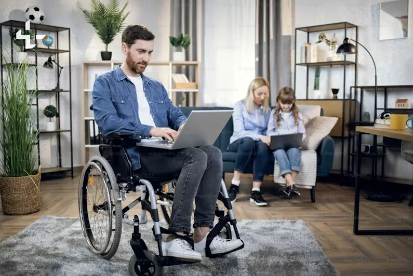 Homme en fauteuil roulant utilisant un ordinateur portable dans un salon, avec une femme et une fille en arrière-plan. Scène illustrant l'accessibilité numérique.